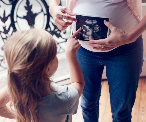 Kleines Mädchen schaut mit einer Schwangeren auf ein Ultraschallbild.
