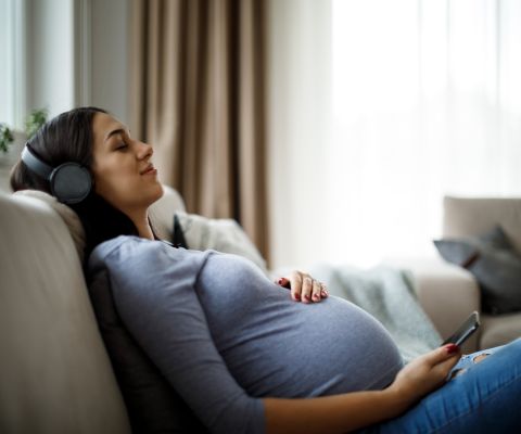 Schwangere mit Kopfhörer relaxt auf dem Sofa