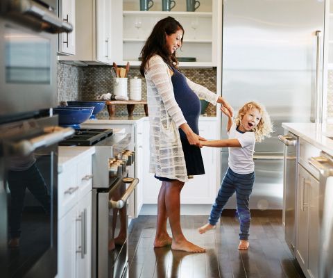 Schwangere und ein kleines Mädchen albern in einer Küche
