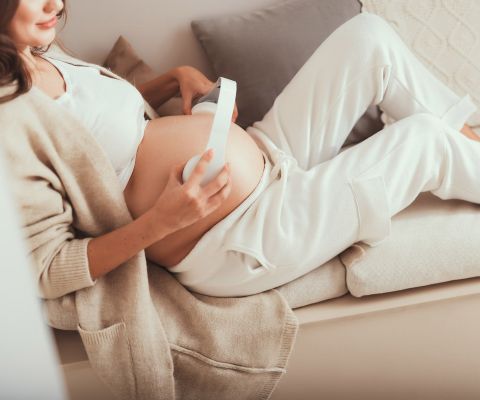 Femme enceinte sur un canapé avec des écouteurs posés sur son ventre