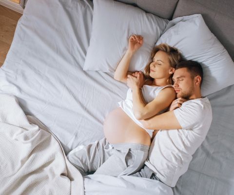Une femme enceinte et un homme endormis, blottis l’un contre l’autre, allongés dans un lit.