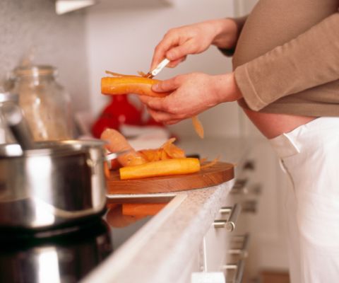 Femme enceinte en train d’éplucher des carottes dans la cuisine