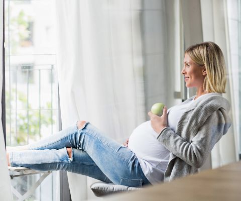 Donna incinta mangia una mela con le gambe sollevate