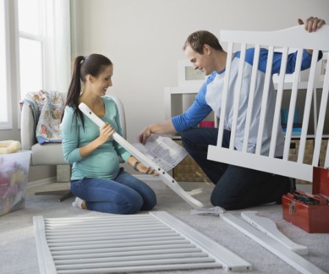 Schwangere und Mann bauen ein Babybett auf