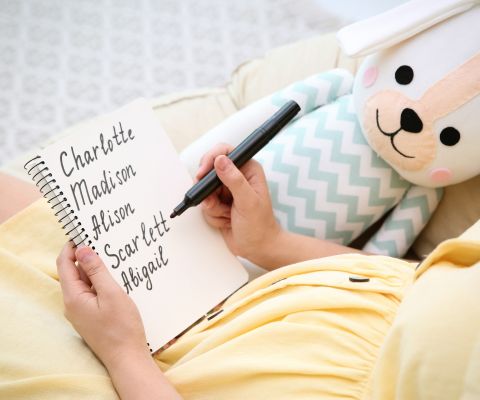 Femme enceinte munie d’un carnet et d’un crayon écrivant des prénoms de petite fille