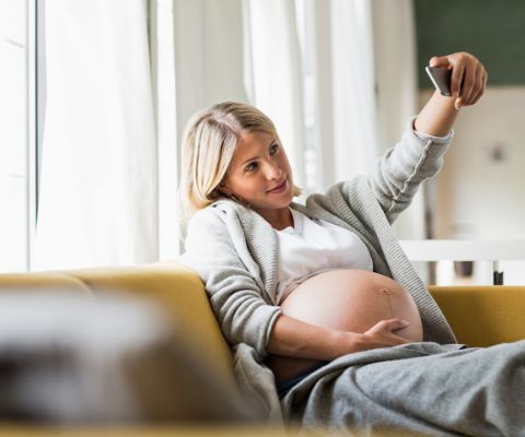 Femme enceinte en train de faire un selfie sur le canapé