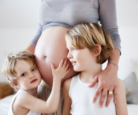 Schwangere mit zwei Kindern, eins horcht am Babybauch