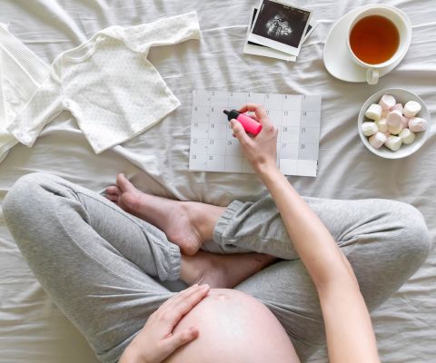 Donna incinta seduta a gambe incrociate evidenza un appuntamento sul calendario