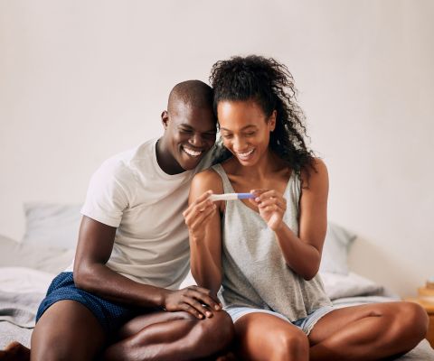 Junges Paar schaut lächelnd auf einen Schwangerschaftstest