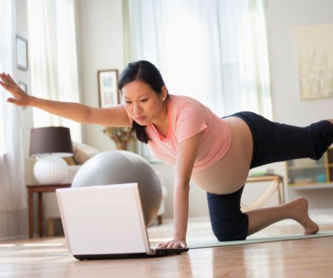 Schwangere macht am Boden Übungen vor dem Laptop