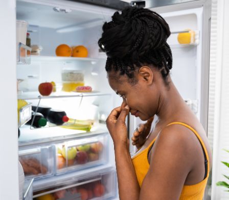 Une femme se bouche le nez devant un réfrigérateur ouvert