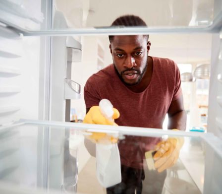 Mann reinigt Kühlschrank mit Kühlschrankreiniger und Schwamm