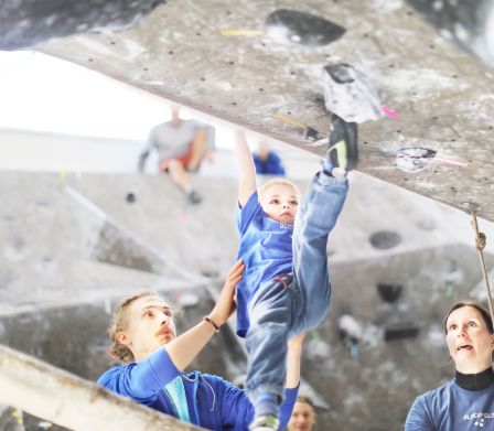 Eltern helfen Sohn beim Klettern in der Boulderhalle