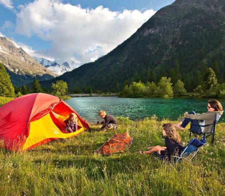 Famille avec une tente rouge devant un lac de montagne