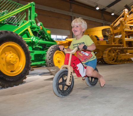 Bambino piccolo su bicicletta senza pedali nel museo dei bulldozer
