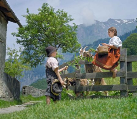 Un bambino e una bambina travestiti da Heidi e Peter con una capretta davanti a una stalla