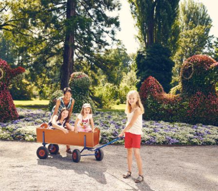 Famille avec un chariot devant des parterres en fleurs dans un parc