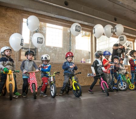 10 Kleinkinder auf ihren bunten Velos und weissen Ballone