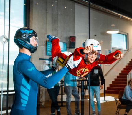 Ein Junge schwebt wie ein Superhero in der Flugkammer, gehalten vom Instruktor