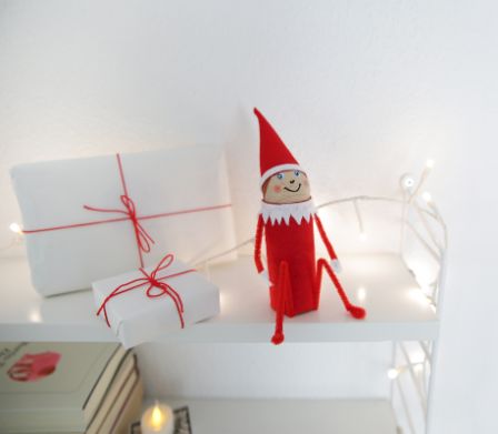 Der sebstgebastelte "Elf on a Shelf" sitzt auf einem dekorierten Regal.