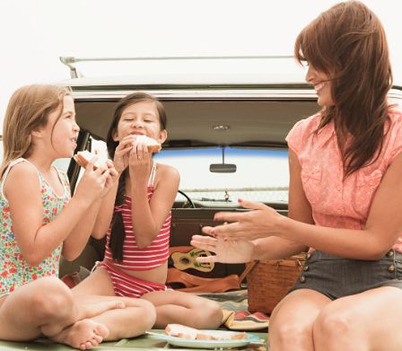 Une femme et deux fillettes mangent sur la surface de chargement d’une voiture