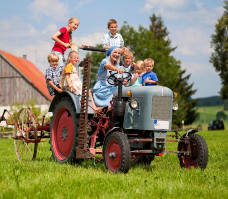 Frau fährt lachend einen Traktor und viele Kinder stehen und sitzen um sie herum