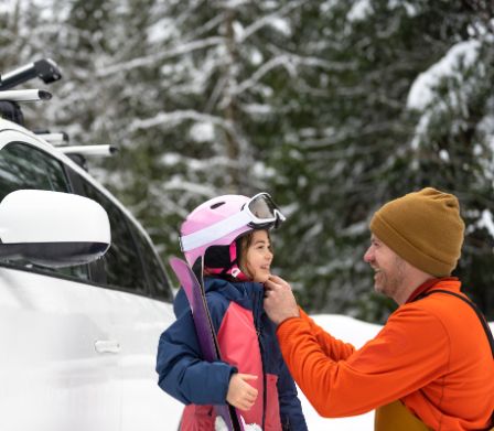 Un père enfile le casque de ski sur la tête de sa fille.