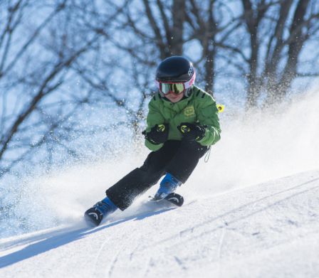 Kind fährt auf Skiern rasant einen Hang hinunter