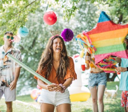 Junge Frau in geschmückten Garten versucht lachend eine Piñata zu schlagen