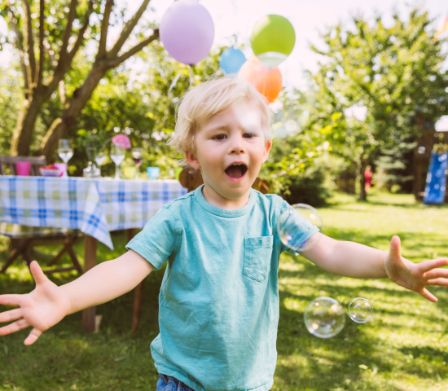 Kind auf einem Gartenfest läuft Seifenblasen hinterher