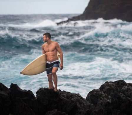Junger Mann mit Surfboard vor aufgewühltem Meer