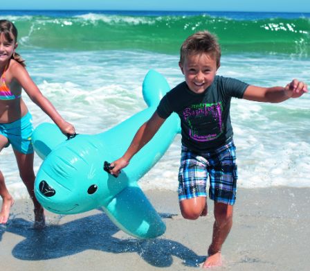 Due bambini corrono con un animale gonfiabile in spiaggia