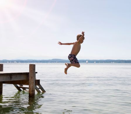 Un ragazzo salta da un pontile nell’acqua di un lago