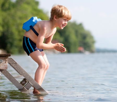 Kleiner Junge mit Schwimmhilfe macht sich bereit zum Sprung in den See