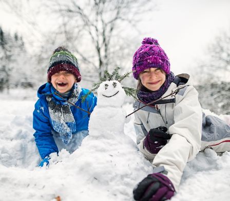 Kinder freuen sich über den Winter und bauen einen Schneemann