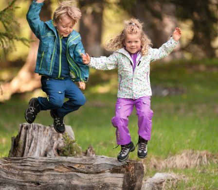 Junge und Mädchen in Wanderausrüstung springen von einem Baumstamm