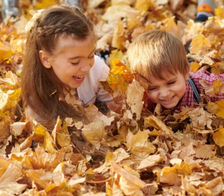 Deux enfants allongés sur le ventre dans un tas de feuilles d’automne