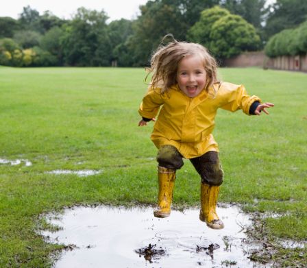 Una bambina con abbigliamento da pioggia si diverte a saltare in una pozzanghera