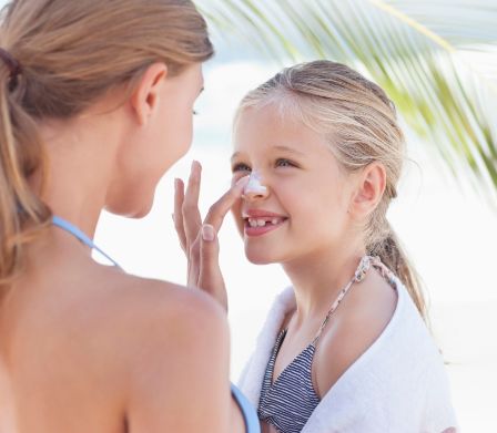 Donna in spiaggia mette la crema sul viso di una bambina