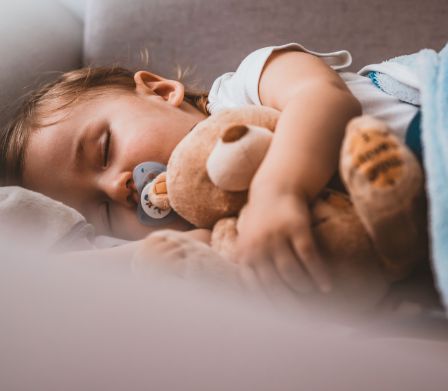Kind schläft mit Teddybär im Arm