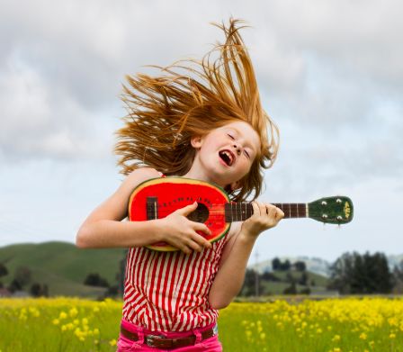 Mädchen vor Wiese hüpft und spielt auf Kindergitarre