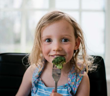 Consigli contro lo spreco alimentare: bambina che mangia broccoli 