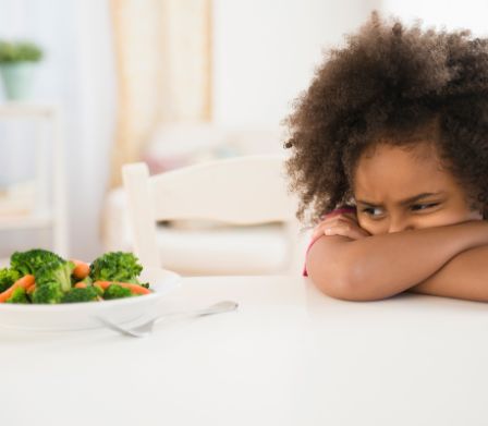 Une enfant regardant d’un œil méfiant une assiette de légumes