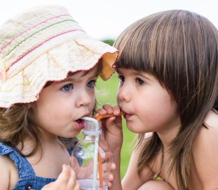 Zwei kleine Mädchen trinken mit Strohhalmen gemeinsam aus einer Flasche
