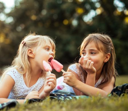 Due bambine mangiano un gelato sedute sul prato 