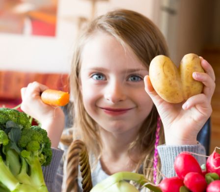 Bambina che mostra sorridente una patata a forma di cuore e una carota