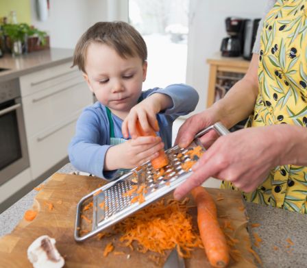 Bambino che aiuta la mamma a grattugiare le carote