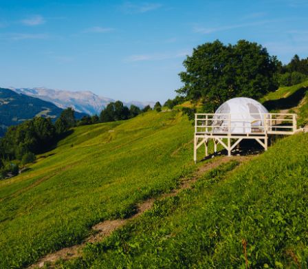 Bubble-Hotel auf grüner Wiese vor Berglandschaft