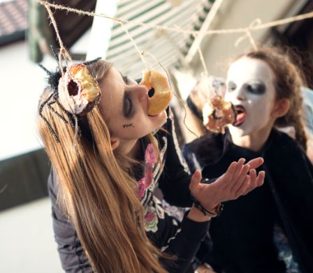 Divertimento di Halloween: delle bambine cercano di mangiare donut appesi a un cordoncino