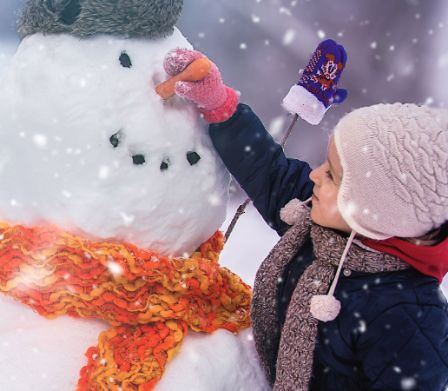 Kind befestigt eine Möhre als Nase an einem Schneemann